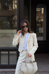 a lady wears a beige tweed boxy crop jacket with matching pants an black sunglasses